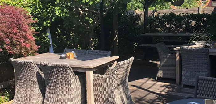 Terras in de tuin met grijze loungezetels en een houten tafel in de zon